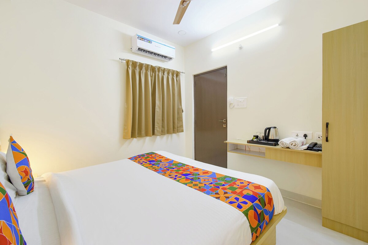 A hotel room with a bed, an air conditioning unit, a door, and a small table with a kettle and a phone.