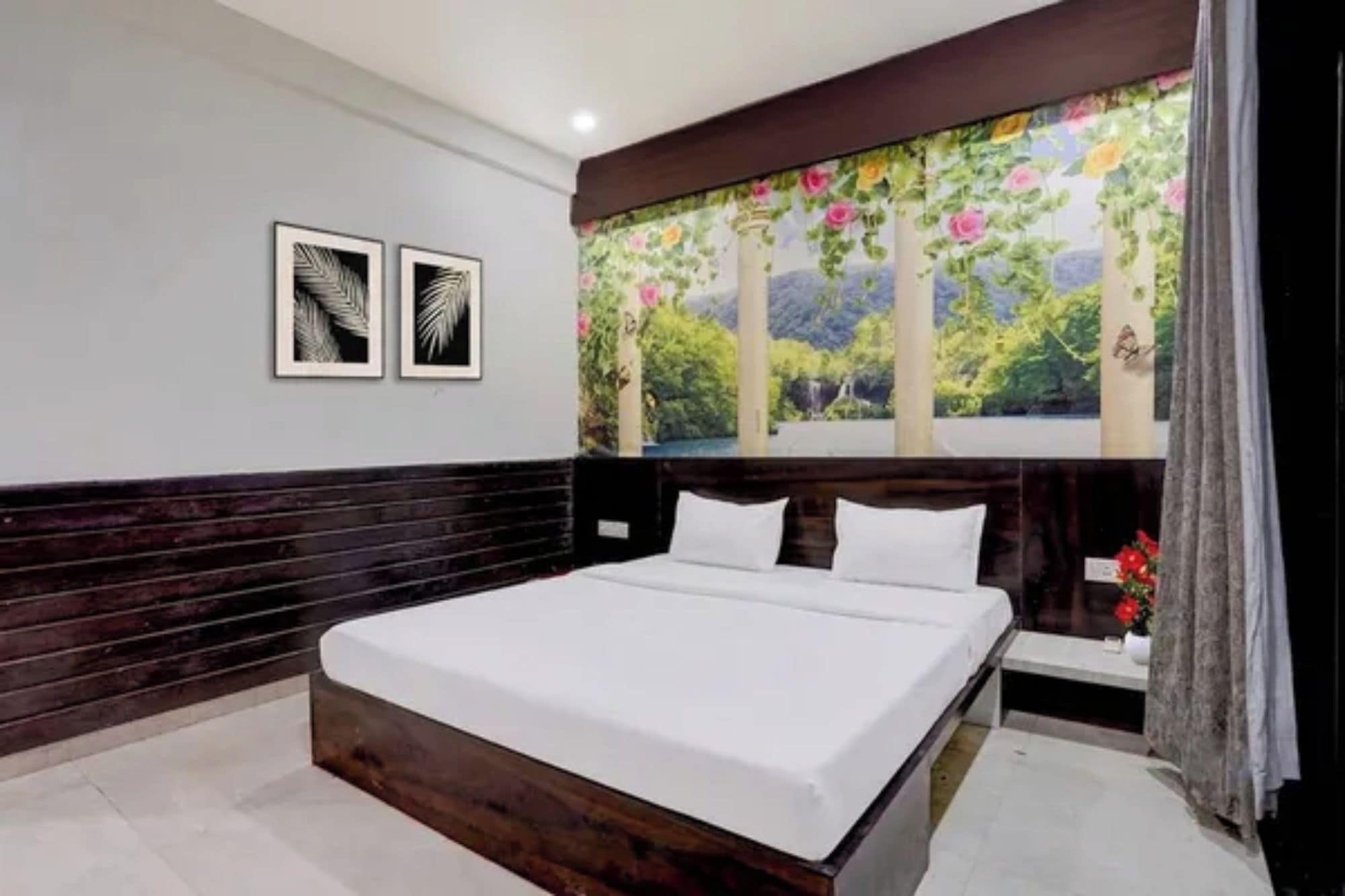 Un dormitorio con una cama grande, un cabecero de madera oscura, una mesita de noche y un mural floral en la pared.