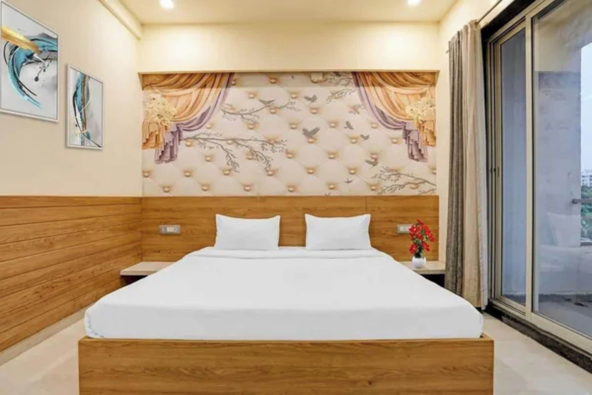 Habitación de hotel con cabecera de madera, cama con ropa blanca, mesita de noche con un jarrón de flores y vista a través de un gran ventanal.