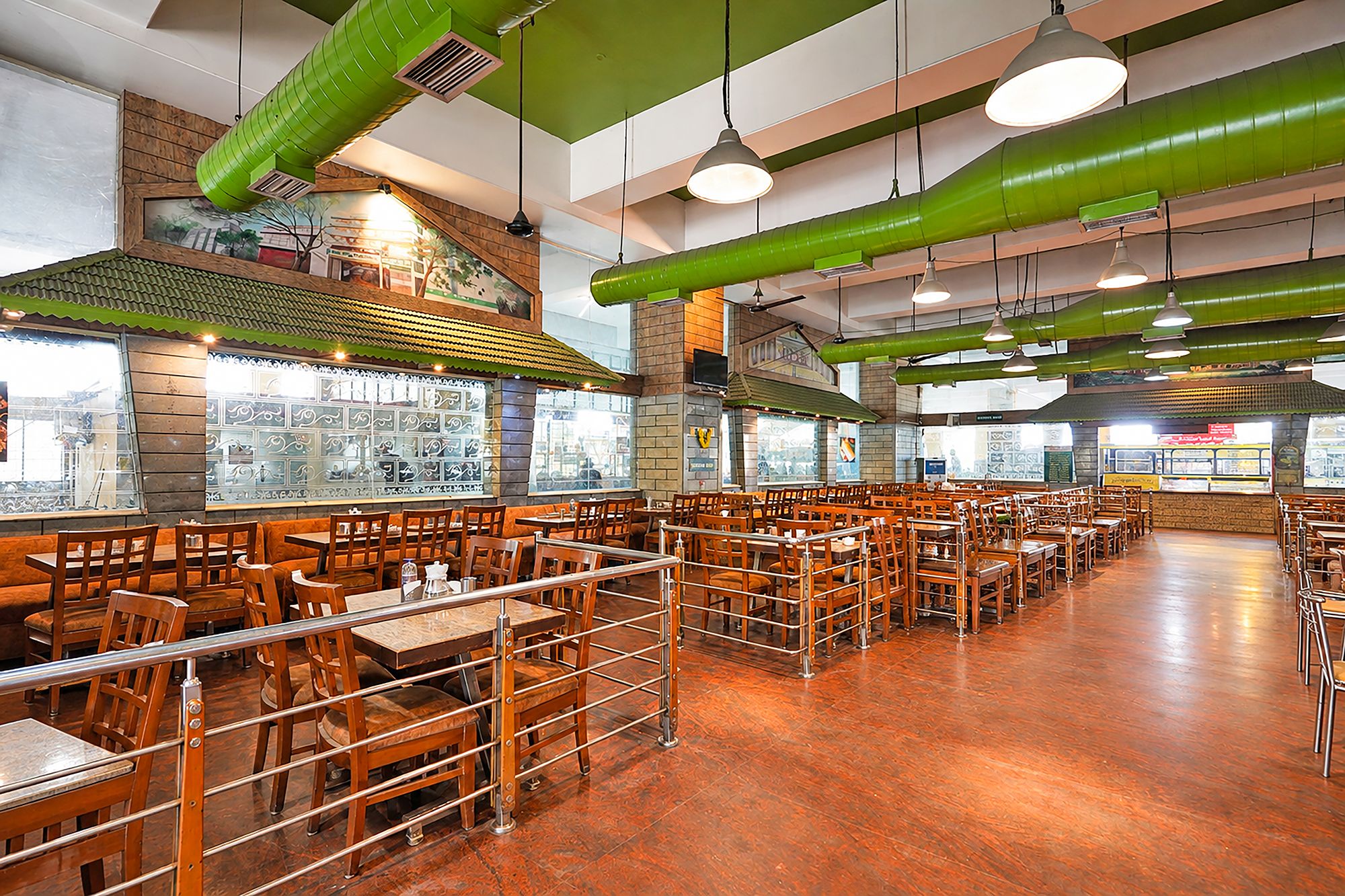 Un restaurante amplio con techos altos, conductos verdes y diferentes opciones de asientos, incluyendo mesas y cabinas.