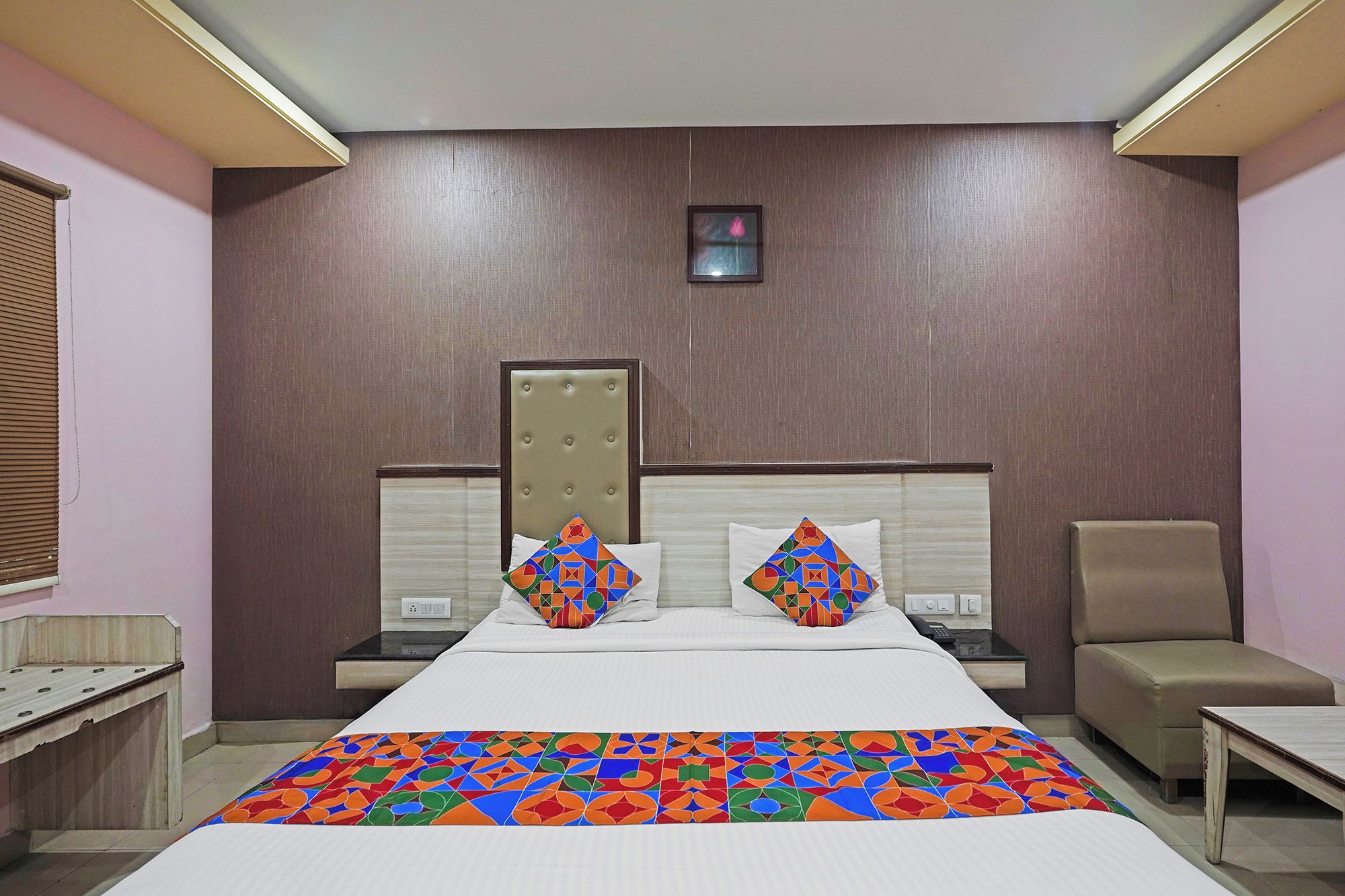 A hotel room with a large bed, two nightstands, a chair, and a small table.