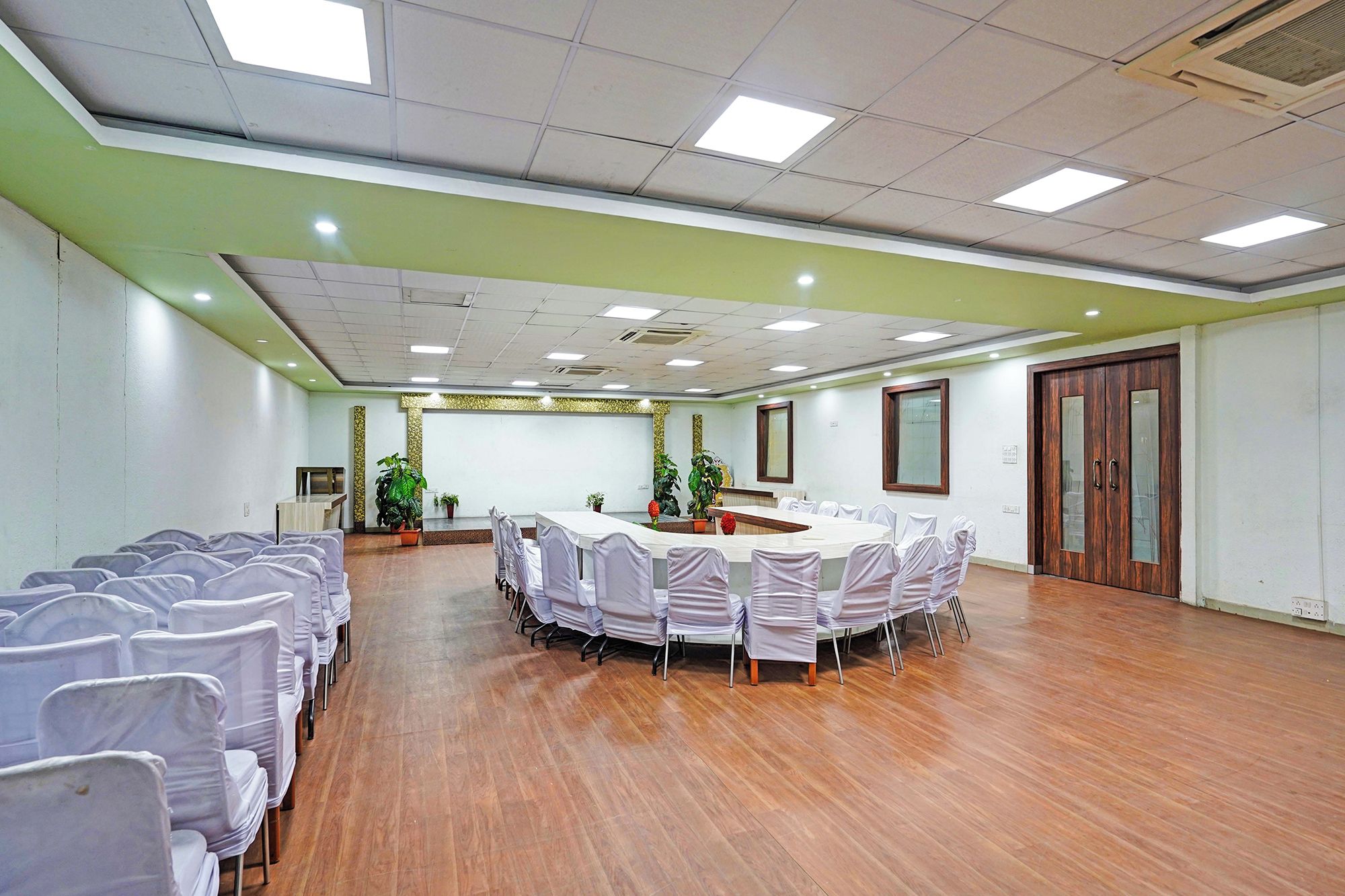 Un salón de conferencias con una mesa larga rodeada de sillas, piso de madera y una pared de acento verde.