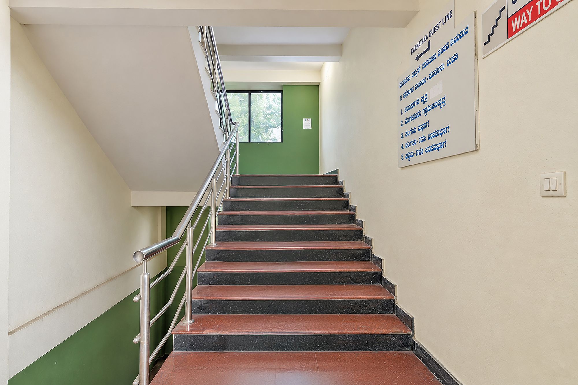 Una escalera con barandillas metálicas que conduce a una puerta verde. Hay un letrero en la pared con texto en un idioma que no es inglés.