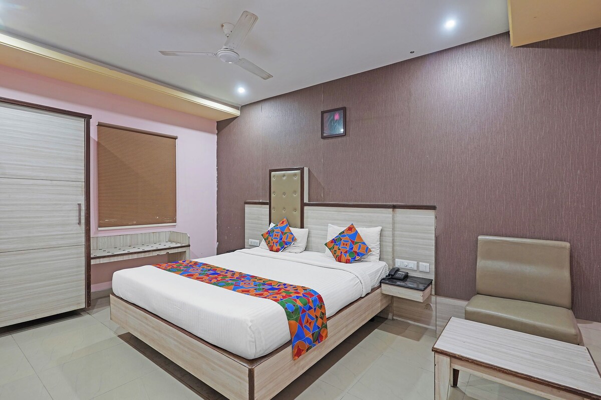 Una habitación de hotel con cama, mesita de noche, silla y ventilador de techo.