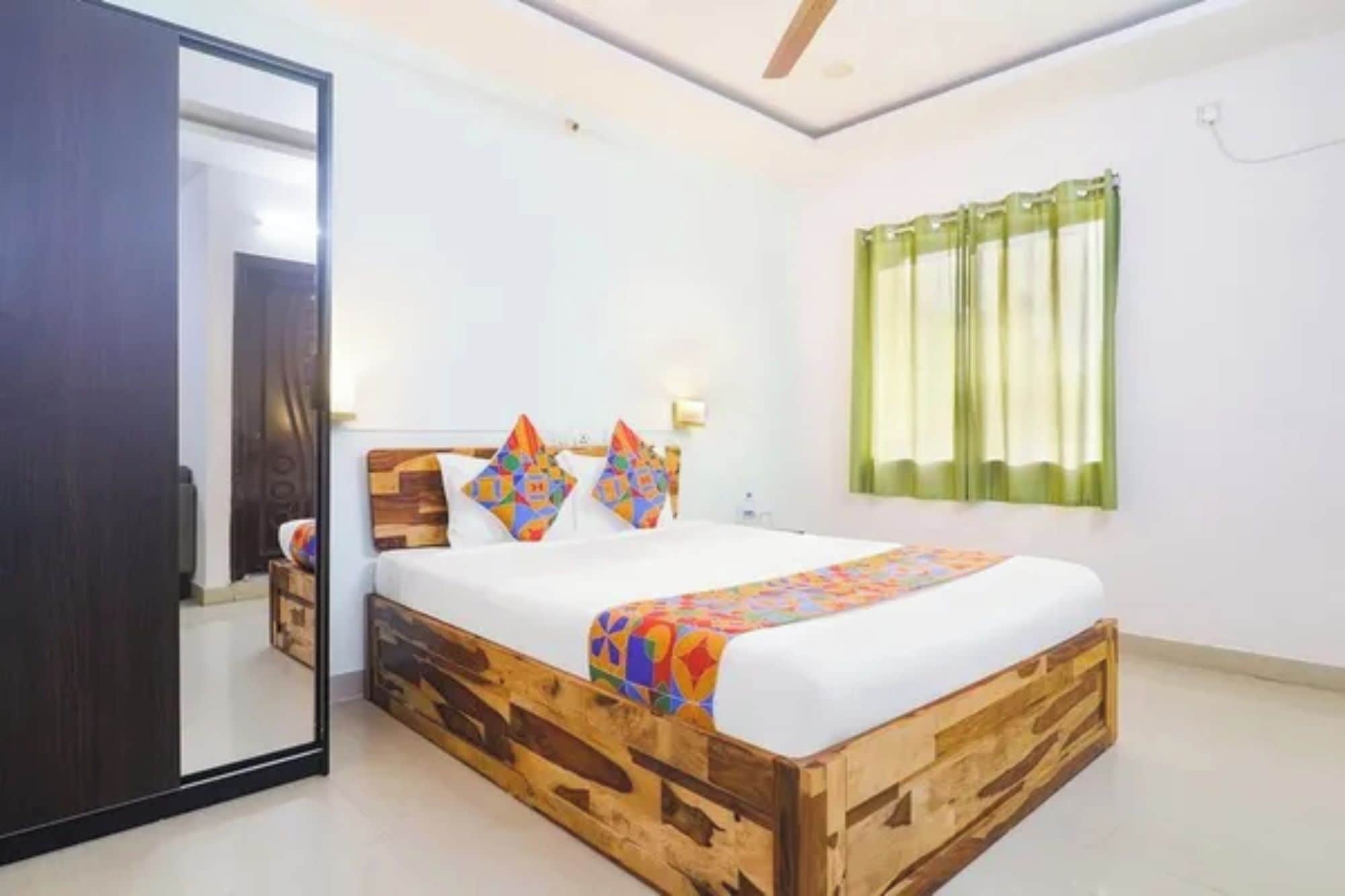 Une chambre à coucher avec un lit en bois, un grand miroir, une table de chevet et une fenêtre avec des rideaux.