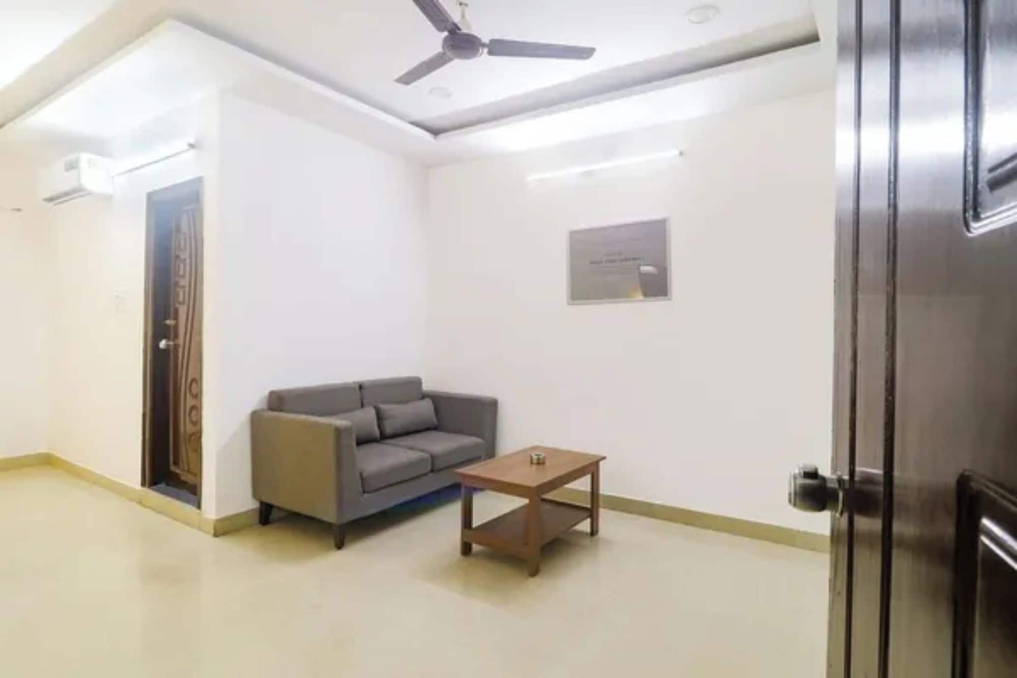 Une pièce avec un ventilateur de plafond, un canapé gris, une petite table en bois et une porte.