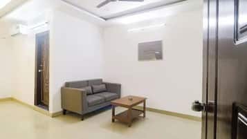 Une pièce avec un ventilateur de plafond, un canapé gris, une petite table en bois et une porte.