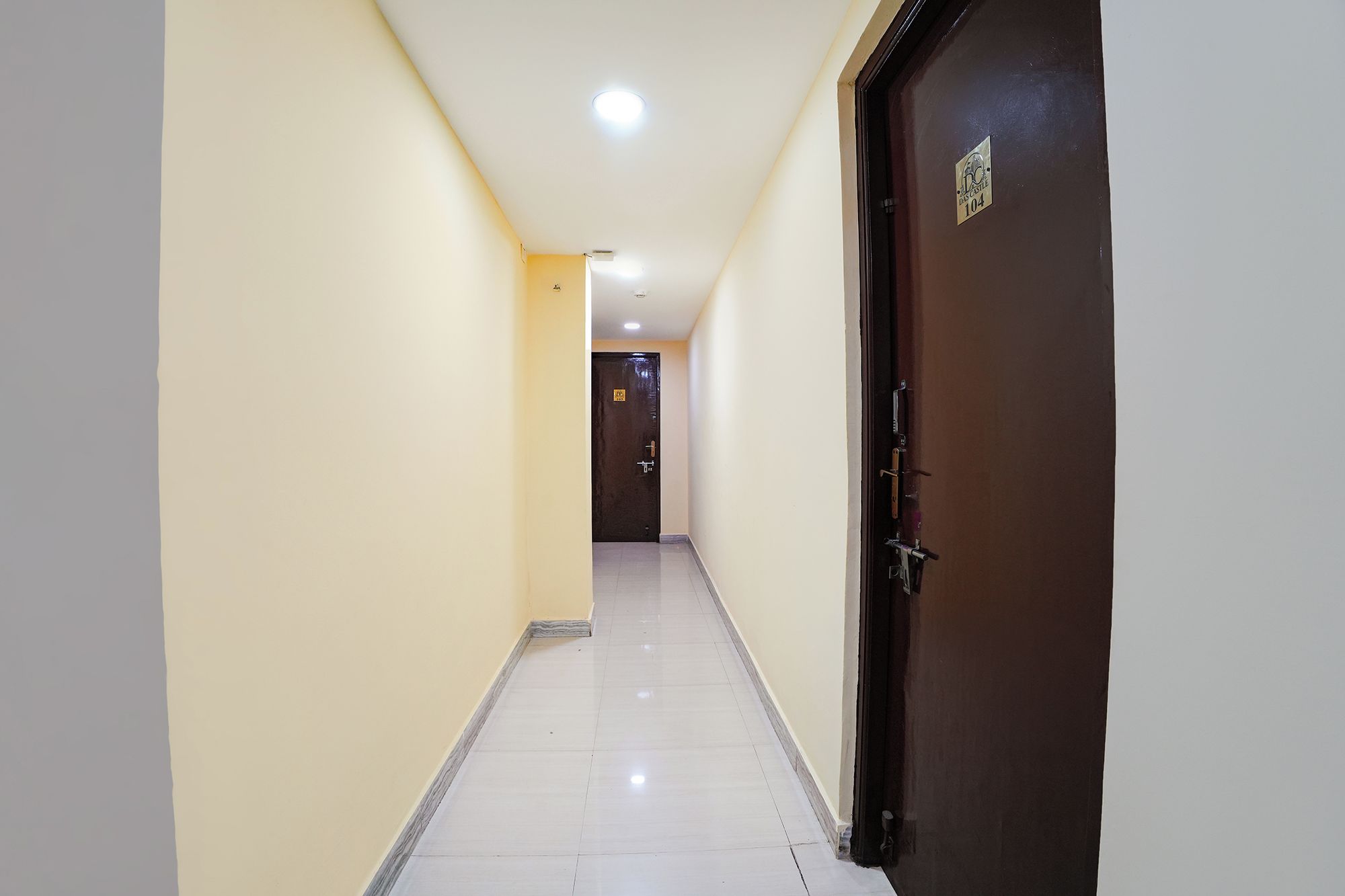 A corridor with a door on the right, a light fixture on the ceiling, and a door at the end.