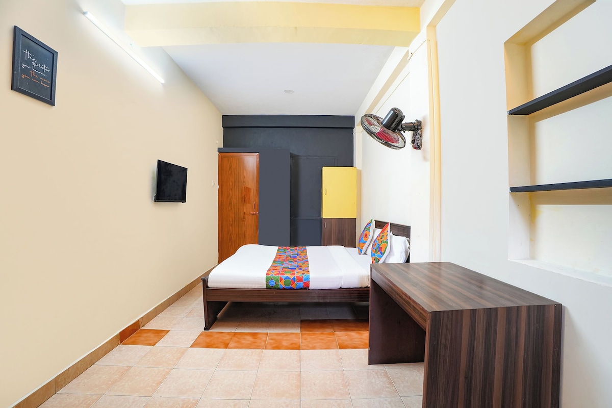 A compact hotel room with a bed, bedside table, and a small desk.