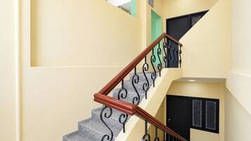 Una escalera con barandilla de madera y barandales de metal negro, que conduce a un rellano con una puerta negra y una ventana con celosía decorativa.