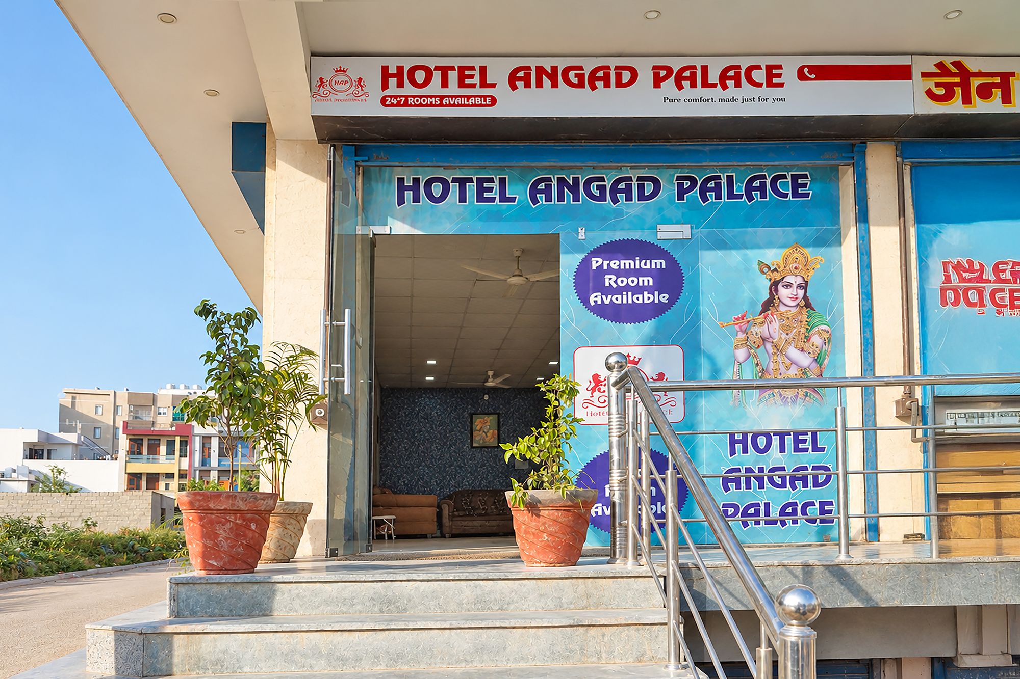 La entrada al Hotel Angad Palace, con un cartel que indica habitaciones disponibles las 24 horas y una opción de habitación premium.