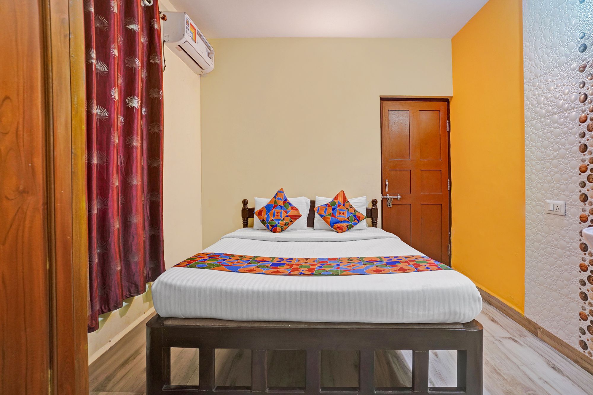 A bedroom with a bed, pillows, a wooden bench, a door, and an air conditioning unit.