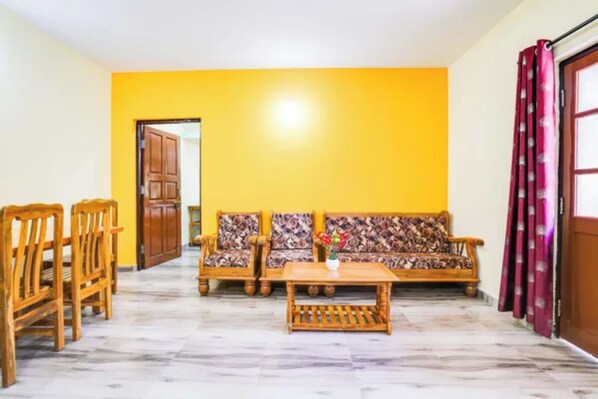 Una sala de estar con un sofá, sillas de madera, una mesa de centro y una puerta.