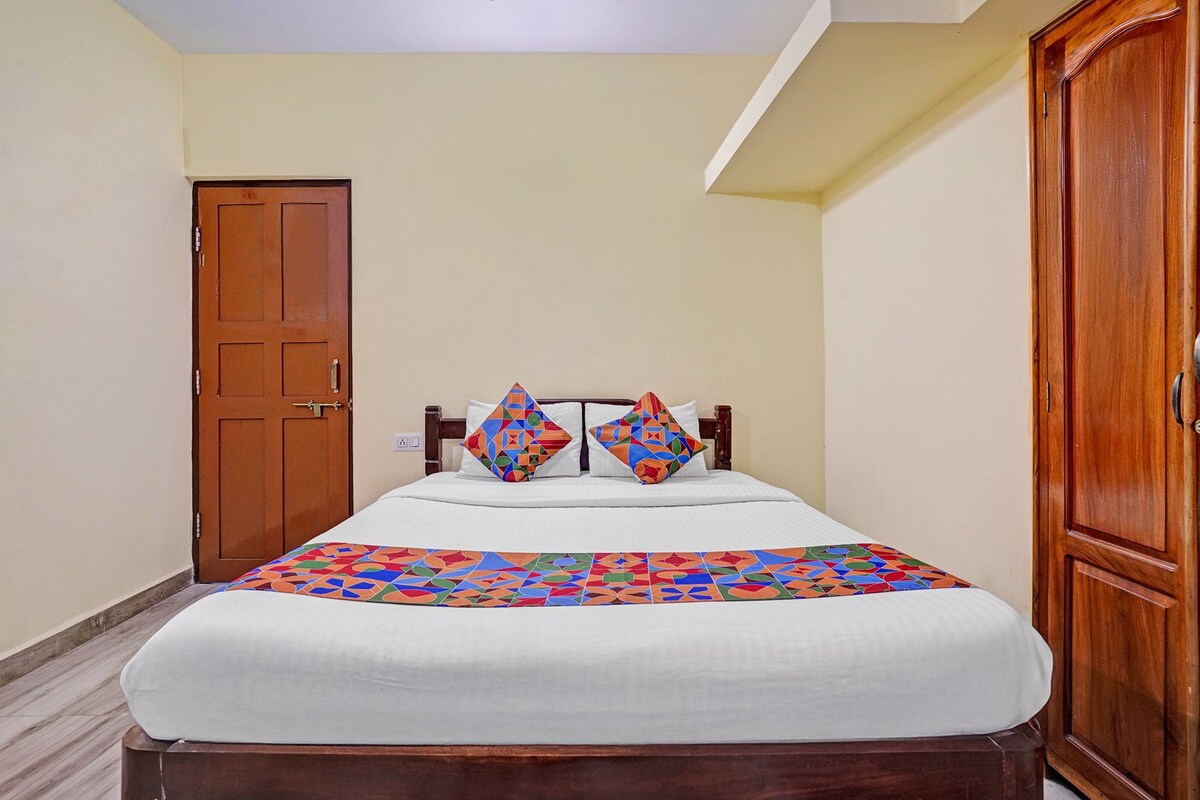 A single bed with a patterned bedspread, two pillows with geometric designs, a wooden headboard, and a wooden wardrobe with a door.