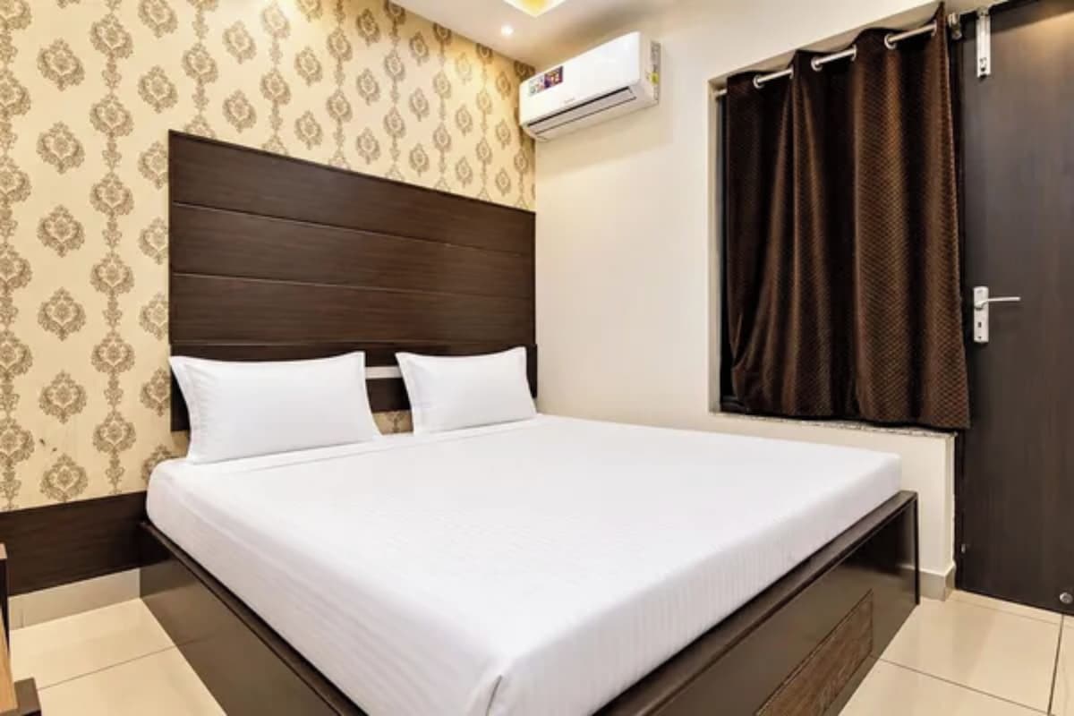 A hotel room with a large bed, a headboard, a window with curtains, and an air conditioning unit.