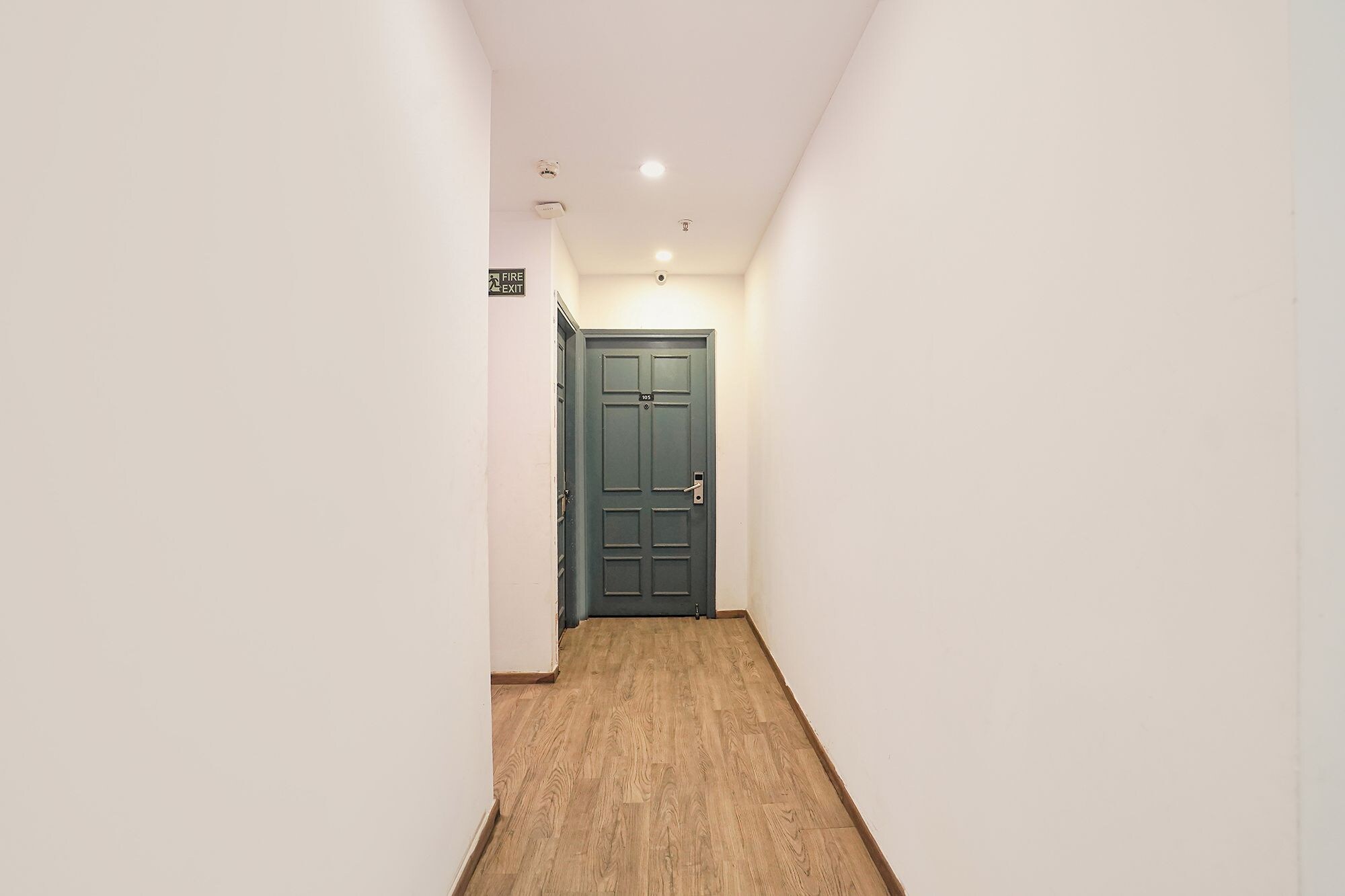 A narrow hallway with a wooden floor and a green door at the end.