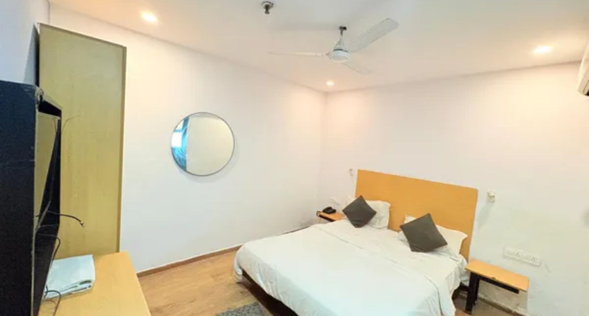 Ett hotellrum med en säng, sängbord, en spegel, en takfläkt och en tv.