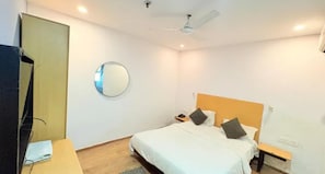 Una habitación de hotel con cama, mesitas de noche, espejo, ventilador de techo y televisor.
