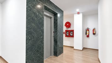A hallway with a marble wall, a door, and a fire extinguisher mounted on the wall.