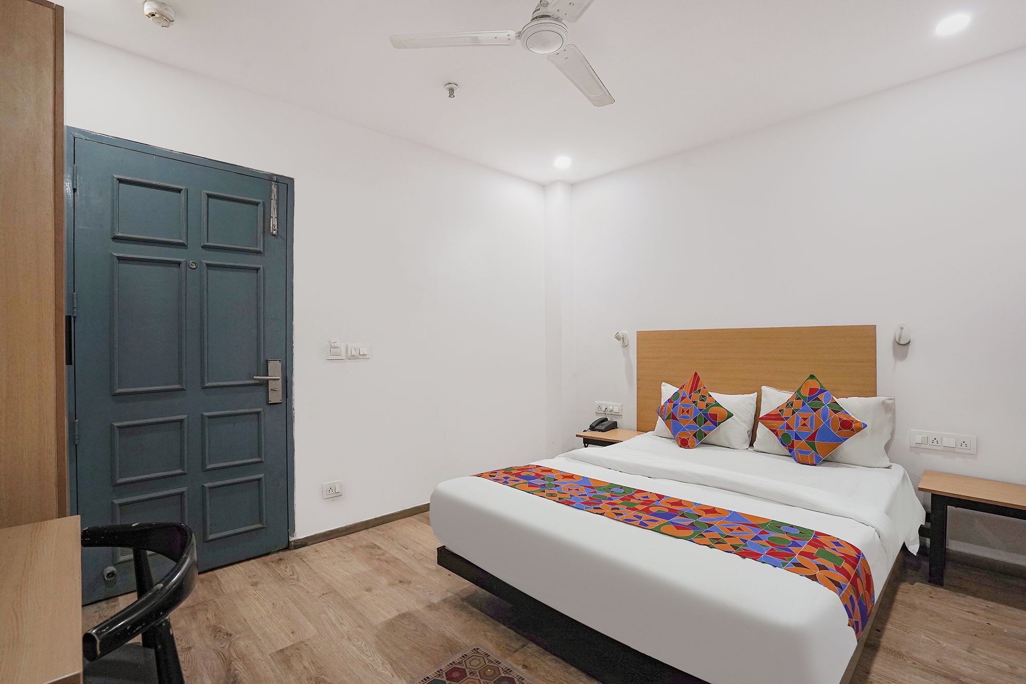 Habitación de hotel con cama, escritorio, silla, ventilador de techo y puerta.