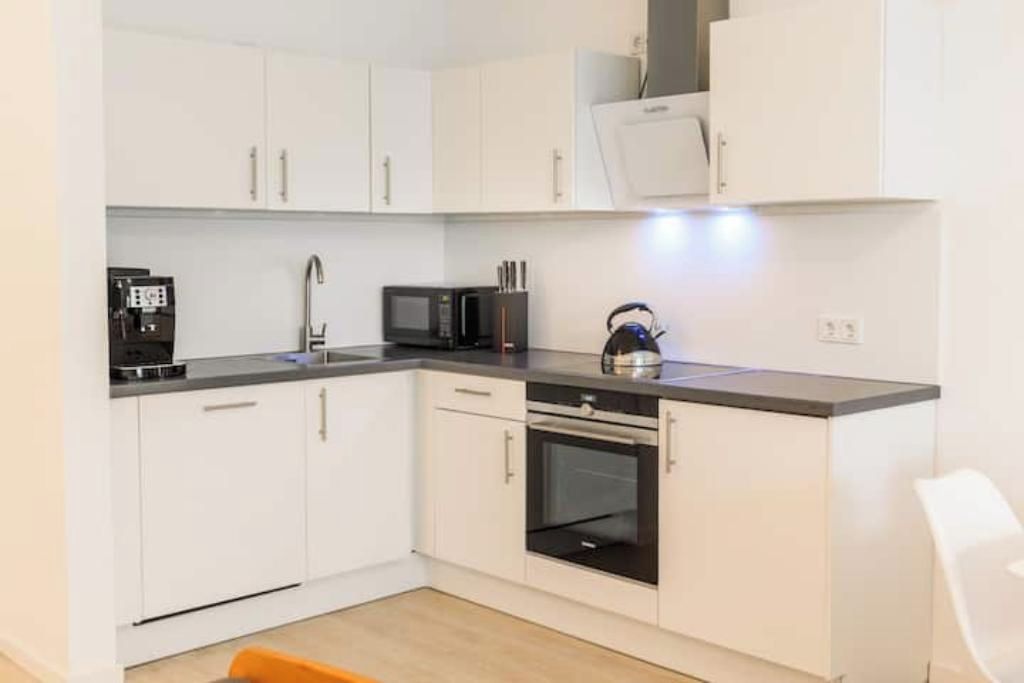 A compact kitchen with white cabinets, a microwave, an oven, and a coffee machine.