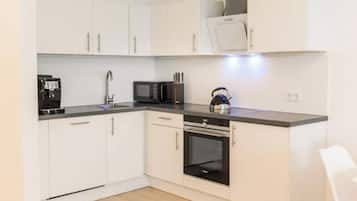 A compact kitchen with white cabinets, a microwave, an oven, and a coffee machine.