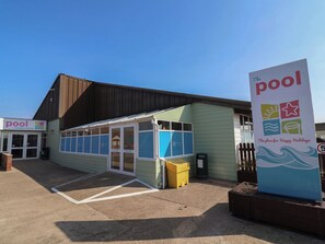 A building with a sign reading 'The Pool' and another sign for 'Golden Sands.' There is a covered area with a bench and a trash bin. - Beach Fields 45 (Rhyl)