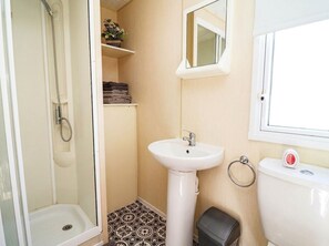 A bathroom with a shower, sink, toilet, and a small window. - Beach Fields 45 (Rhyl)