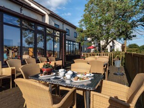 An outdoor dining area with wicker furniture and a table set for a meal. - Goldfinch (Newton Abbot)