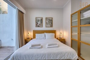Quarto de hotel com uma cama grande, duas mesas de cabeceira, uma porta de vidro deslizante e duas obras de arte emolduradas na parede.