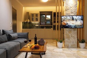 A modern living room with a sofa, a coffee table with fruit and wine, a TV, and a stone pillar. - Koukounari Apartment in Downtown Chania (Chania)