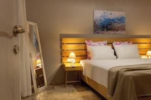 A hotel room with a bed, two bedside lamps, a nightstand, a mirror, and a painting on the wall. - Koukounari Apartment in Downtown Chania (Chania)