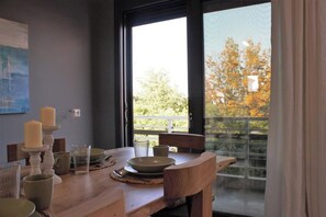 Ein Essbereich mit Tisch für zwei Personen, ein Fenster mit Blick auf Bäume und ein Gemälde an der Wand.