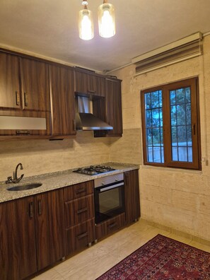 Una cocina con armarios de madera, una campana extractora de acero inoxidable, horno empotrado, encimera de granito y ventana con vista a árboles.