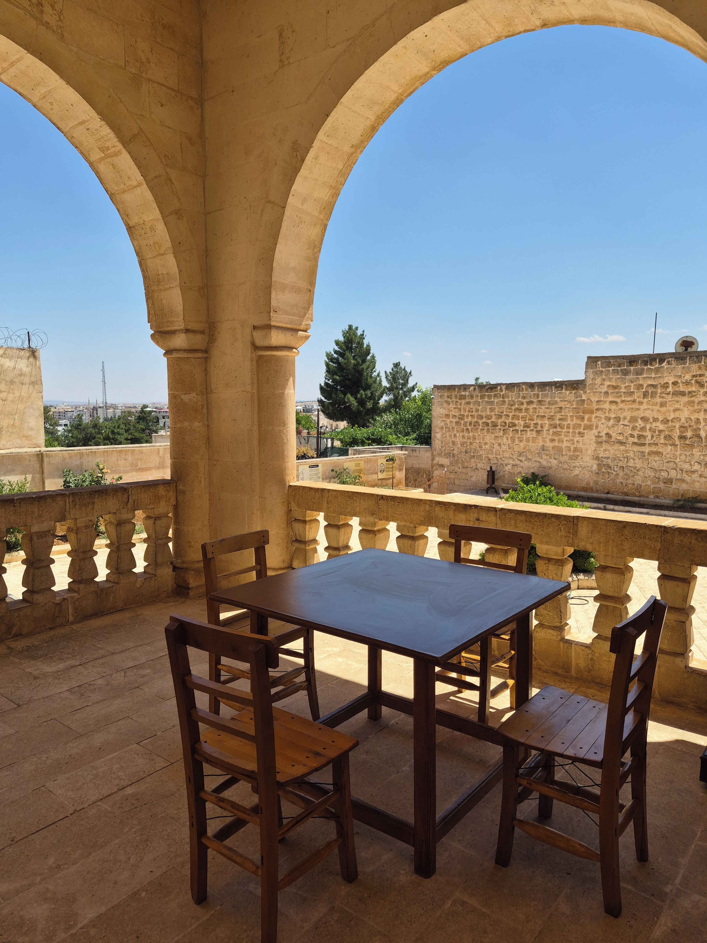 An outdoor patio with a table and chairs, stone arches, and a view of a cityscape.