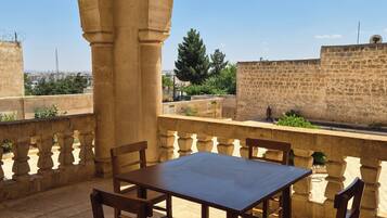 An outdoor patio with a table and chairs, stone arches, and a view of a cityscape.