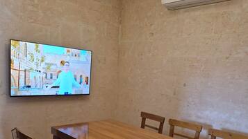 Un coin repas avec une table et des chaises en bois, un téléviseur fixé au mur et un appareil de climatisation.
