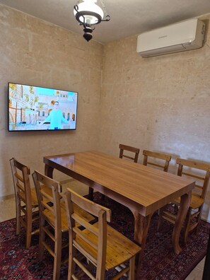 En matplats med ett träbord och stolar, en tv som är monterad på väggen och en luftkonditioneringsanläggning.