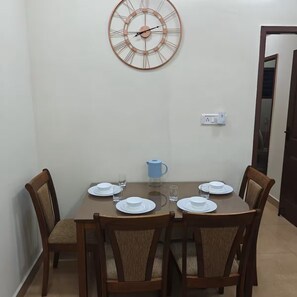 A dining area with a round table, four chairs, a wall clock, and a kettle. - Maison Peach.  2BHK near Apollo, Sankara Nethralaya in the Heart of the city! (Chennai)