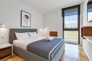 A modern bedroom with a bed, a nightstand, a large window, and a wall-mounted artwork. - Luxury Spa Villa • Heated Pool, Jacuzzi & Sauna (Raštević)