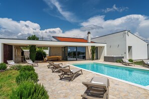 A modern house with a swimming pool, lounge chairs, and a stone patio. - Luxury Spa Villa • Heated Pool, Jacuzzi & Sauna (Raštević)