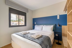 A hotel room with a bed, a window, a blue accent wall, and a view of buildings outside. - Max by Bhomy (São Paulo)