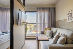 A modern hotel room with a sofa, a small table, a TV, and a balcony with curtains. - Max by Bhomy (São Paulo)