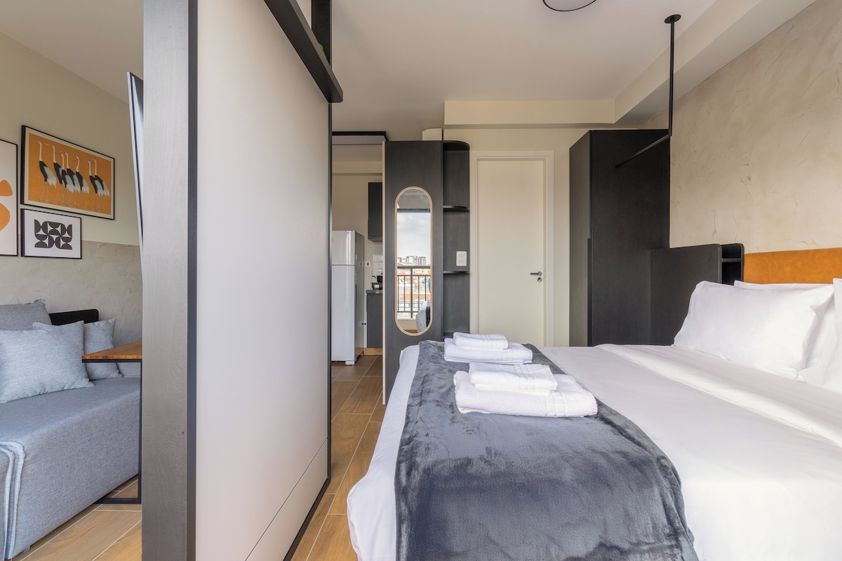 A hotel room with a bed, a sofa, a mirror, and artwork on the wall.