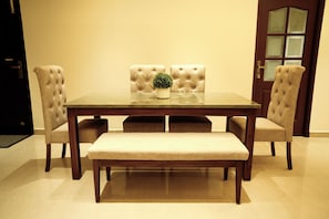 A dining room with a rectangular table, four upholstered chairs, a bench, and a potted plant. - LA COAST (4 bedrooms) (Tirupporur)