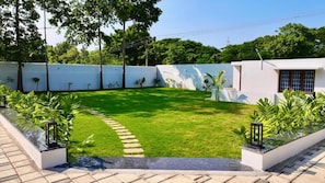 Un jardín bien cuidado con un sendero pavimentado, rodeado por un muro blanco y diversas plantas.