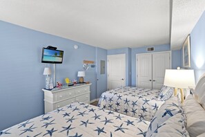 Une chambre avec deux lits, une télévision, une commode et une porte.