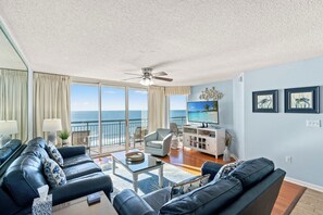 Un salon avec vue sur l’océan, un ventilateur de plafond, un téléviseur à écran plat et un meuble de rangement blanc.
