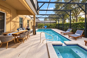 A pool area with a sunken hot tub, lounge chairs, and a dining table with chairs. - PROMO 5 BR Villa | Games | Pool | Near Disney - by Blue Sky Villas (Davenport)