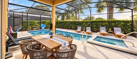 A pool area with lounge chairs, a table, and a glass-enclosed structure.